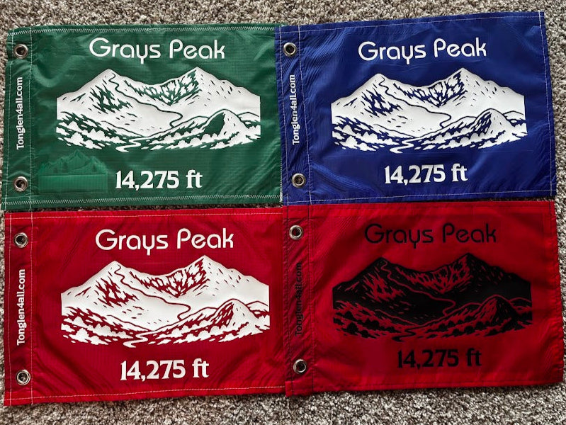 Four fabric flags with Grays Peak mountain details and measurements on a carpeted floor.