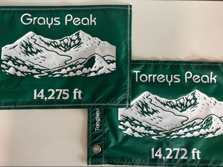 Two green mountain peak flags with white text and illustrations on a neutral background
