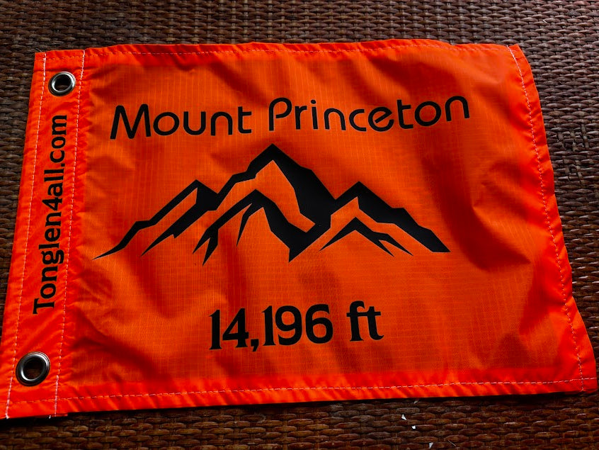 Orange flag with Mount Princeton and height measurement on a brown surface